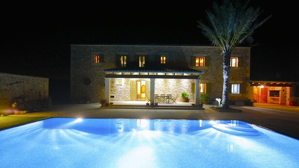 A poolside view of a stone building with a covered patio area and a pool.