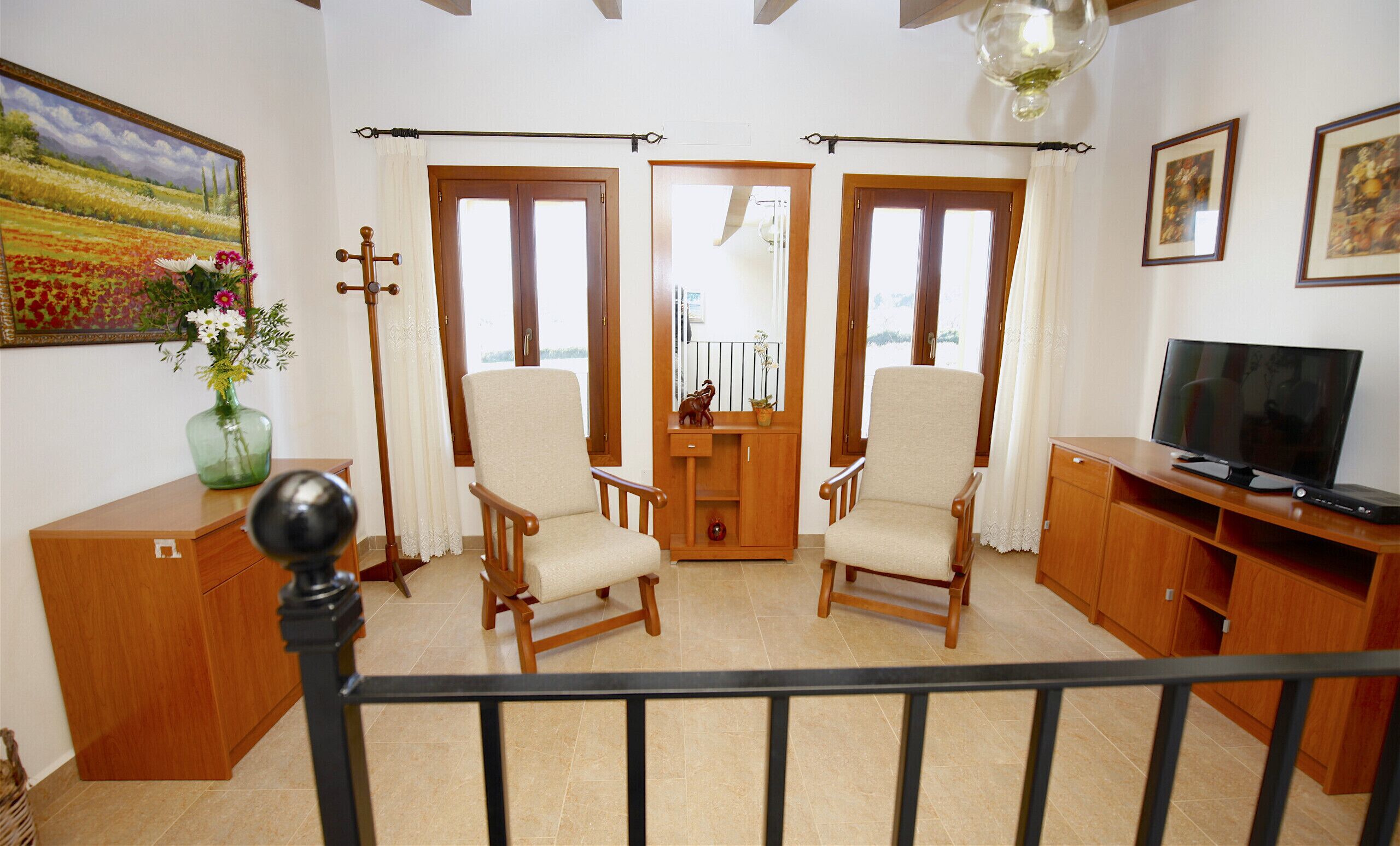 A living room with two armchairs, a wooden cabinet, a television, and a painting on the wall.