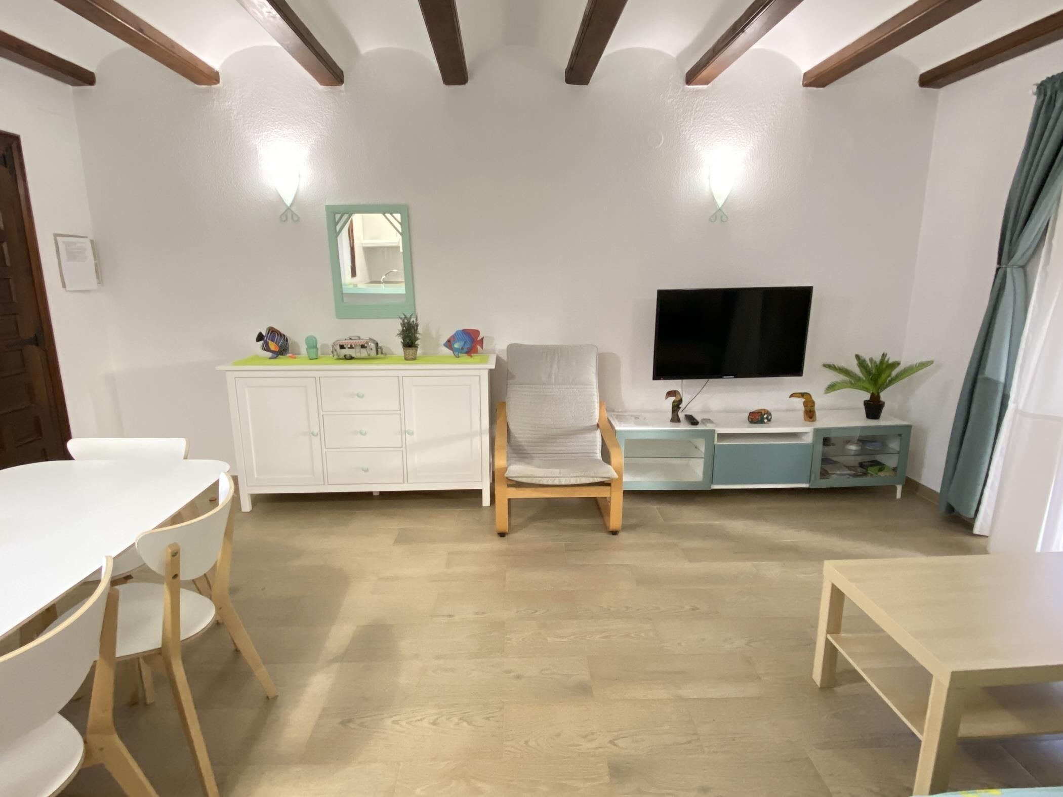 Un salon avec un meuble blanc, un fauteuil, un téléviseur et une petite table.