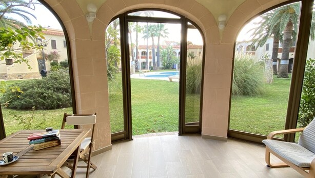 Un patio con tavolo e sedie, vista su una piscina e un edificio con archi sullo sfondo.