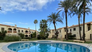 Area piscina con una vasca circolare, palme e un edificio con tetto in tegole.