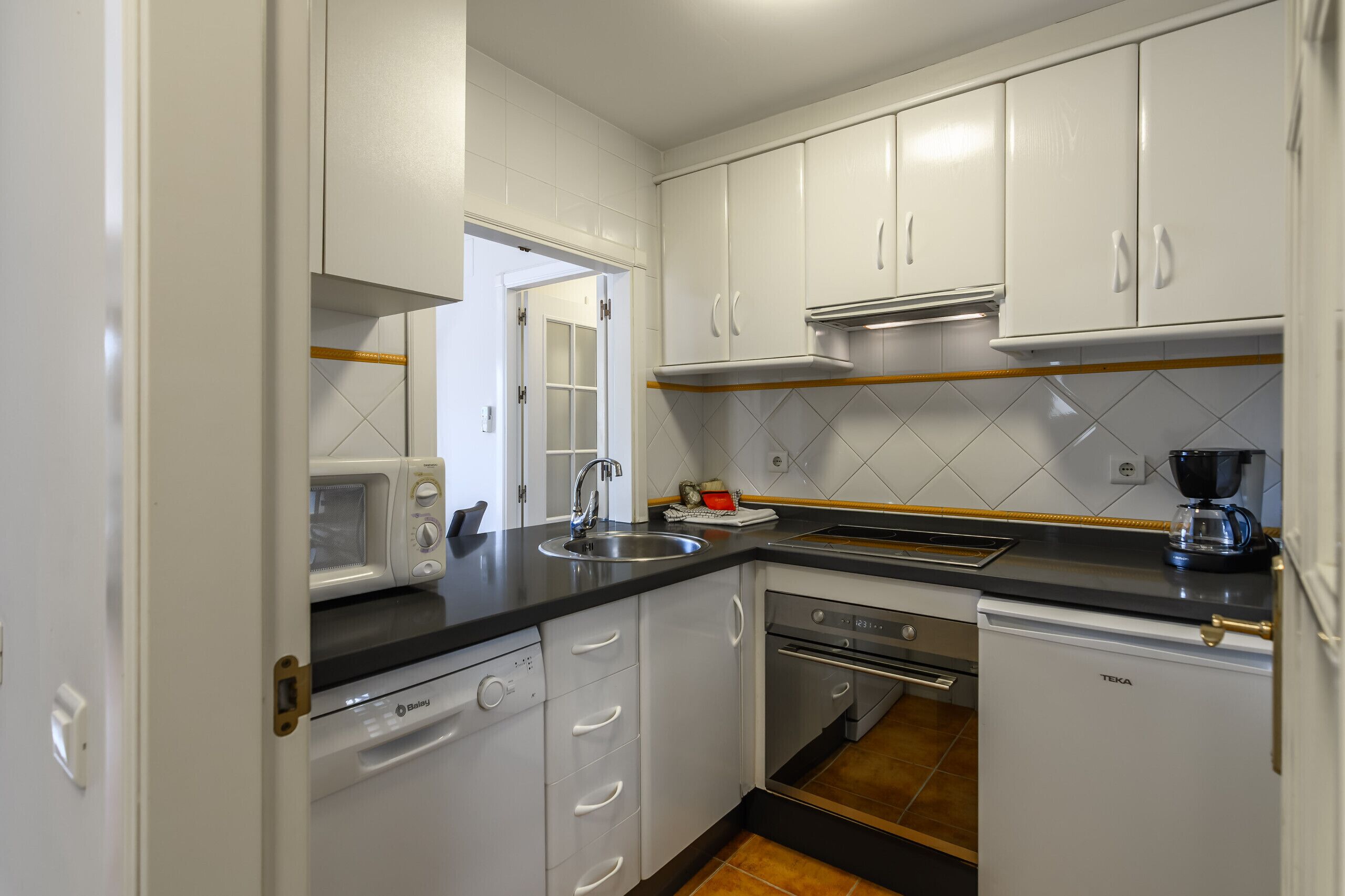 A compact kitchen with white cabinets, a microwave, a coffee maker, and a dishwasher.