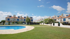 Zona residencial con piscina, casas con techos de tejas rojas y cielo azul despejado.