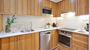 A modern kitchen with wooden cabinets, stainless steel appliances, and a white countertop. - Columbus Apartment, - One Bedroom Apartment, Sleeps 2 (Barcelona)