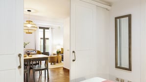 A hotel room with a bed, a dining area with a table and chairs, a chandelier, and a large mirror. - Columbus Apartment, - One Bedroom Apartment, Sleeps 2 (Barcelona)