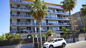 A multi-story residential building with balconies, palm trees, and a white car parked in front. - SOLUXE Apartment - Only Families - Beachfront (Salou)