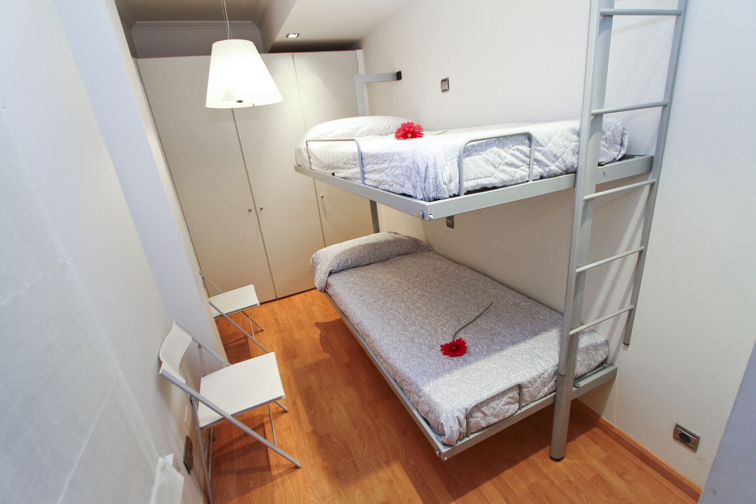 A bunk bed room with a white ceiling, a white desk, and a white chair.