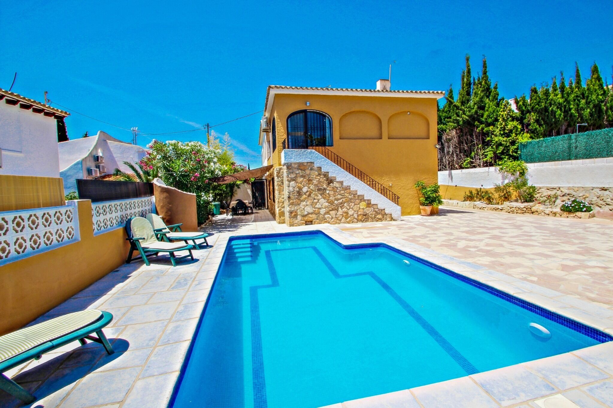 A swimming pool with lounge chairs, a stone staircase, and a yellow building with a window.