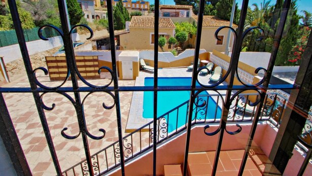 On aperçoit, à travers une grille en métal, un quartier résidentiel avec une piscine, un sol carrelé et un balcon agrémenté de mobilier d’extérieur.