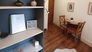 A compact living space with a kitchen area, a dining table with chairs, and a white rug on the wooden floor.