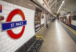 A subway station with a sign for St. Paul's, a tiled wall, a bench, and a train platform.