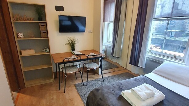 A hotel room with a bed, a desk with chairs, a television, and a window with curtains.
