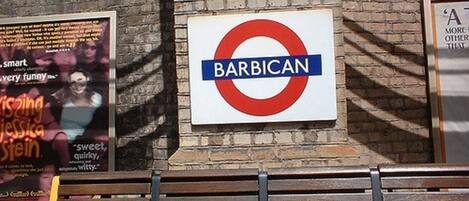 A sign for 'BARBICAN' with a red circle and blue bar design, mounted on a brick wall.