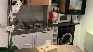 A compact kitchen with wooden cabinets, a stainless steel sink, a microwave, a coffee maker, and a washing machine.