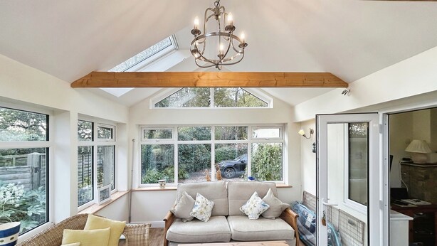 A sunroom with a high ceiling, large windows, a wooden bench, a sofa, and a table.