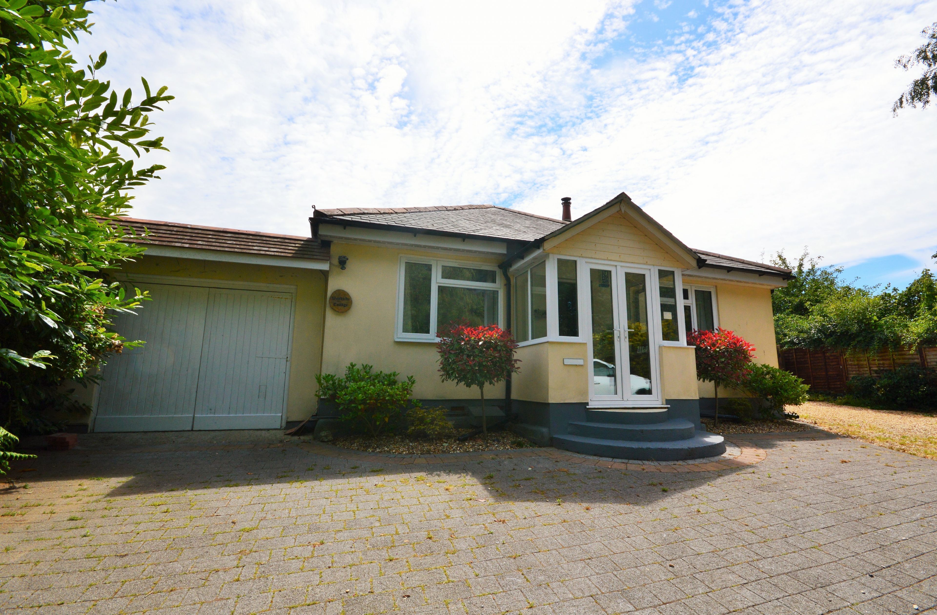 A single-story house with a garage, a front porch, and a small garden area with red flowers.
