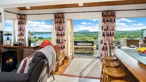 Ein gemütliches Zimmer mit Kamin, einer Couch, einer hölzernen Bank und Blick ins Grüne.