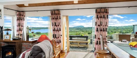 A cozy room with a fireplace, a sofa, a wooden bench, and a view of the countryside.