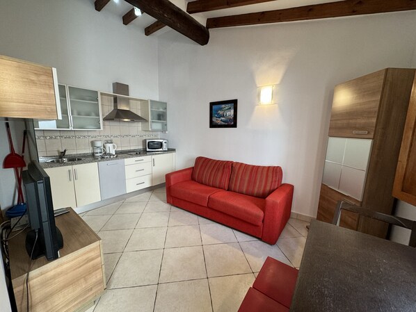 A compact kitchen with a red sofa, a dining table, and a TV on a wooden stand.