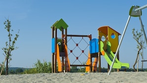 Une aire de jeux avec une structure d’escalade et des toboggans, le tout situé sur une plage de sable.