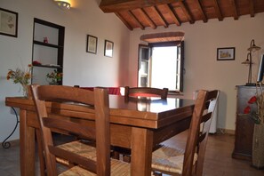 Zona pranzo con tavolo e sedie in legno, una finestra vista e uno scaffale con oggetti decorativi.