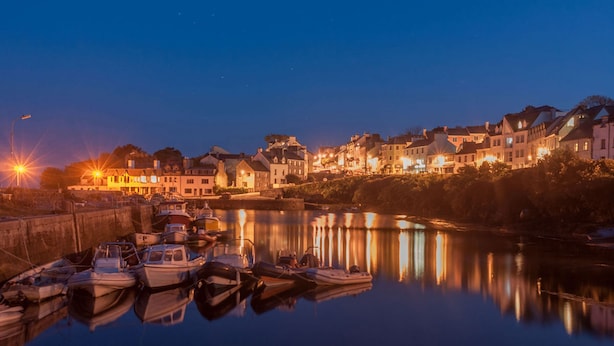 Eine am Wasser liegende Stadt bei Nacht mit vertäuten Booten und beleuchteten Gebäuden.