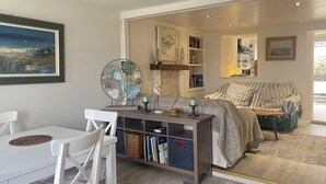Ein gemütliches Wohnzimmer mit einem weißen Tisch, einer Bücherwand, einem grünen Sofa und einem großen Fenster.
