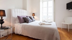 Un dormitorio ordenado con una cama grande, lámparas de noche, un televisor y vistas al exterior.