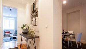 Un comedor moderno con una mesa de vidrio y sillas metálicas, un jarrón con flores sobre un pedestal y una obra de arte en la pared.