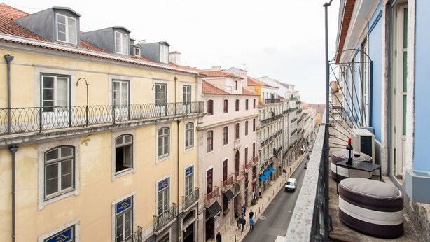 Una calle estrecha flanqueada por edificios con balcones, y automóviles circulando.