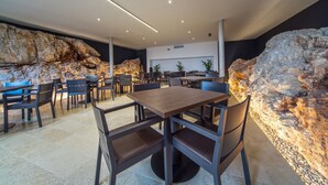 Een moderne eetruimte met een centrale houten tafel en omliggende stoelen, met een achtergrond van textuurrijke rotswanden en inbouwspots.