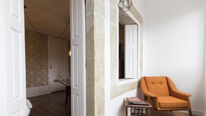 A room with a wooden floor, a white door, a small table with magazines, and an orange chair. - The Brewmaster's House 2 | Studio Deluxe (Porto)