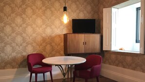 A room with a patterned wallpaper, a wooden cabinet, a television on top, and two red chairs around a round table. - The Brewmaster's House 2 | Studio Deluxe (Porto)