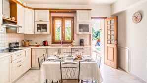 A kitchen with white cabinets, a dining table set for four, and a view of the outdoors through a door. - Private villa with unique panoramic sea views, pool, bbq, 3km to the beach! (Prines)