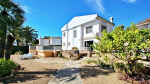 A white two-story house with a stone pathway leading to the entrance, surrounded by greenery and a clear blue sky. - Celia - oceanfront villa in Costa Blanca (Benissa)