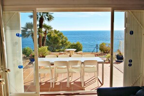 Une terrasse avec une table et des chaises, offrant une vue panoramique sur la mer et les palmiers.
