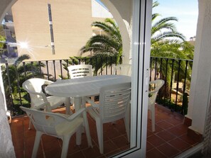 Enjoy a tranquil balcony with a table and chairs, offering a view of palm trees and a nearby building.