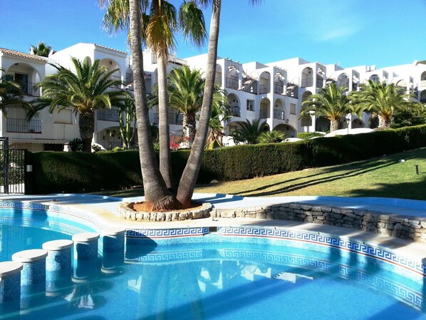 Relax by the pool surrounded by palm trees and a stone wall.