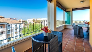 Un balcon avec une table et des chaises, un vase rempli de fleurs et une vue sur les bâtiments.