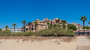 Ett hotell vid kusten med flera byggnader, en sandstrand och palmer.