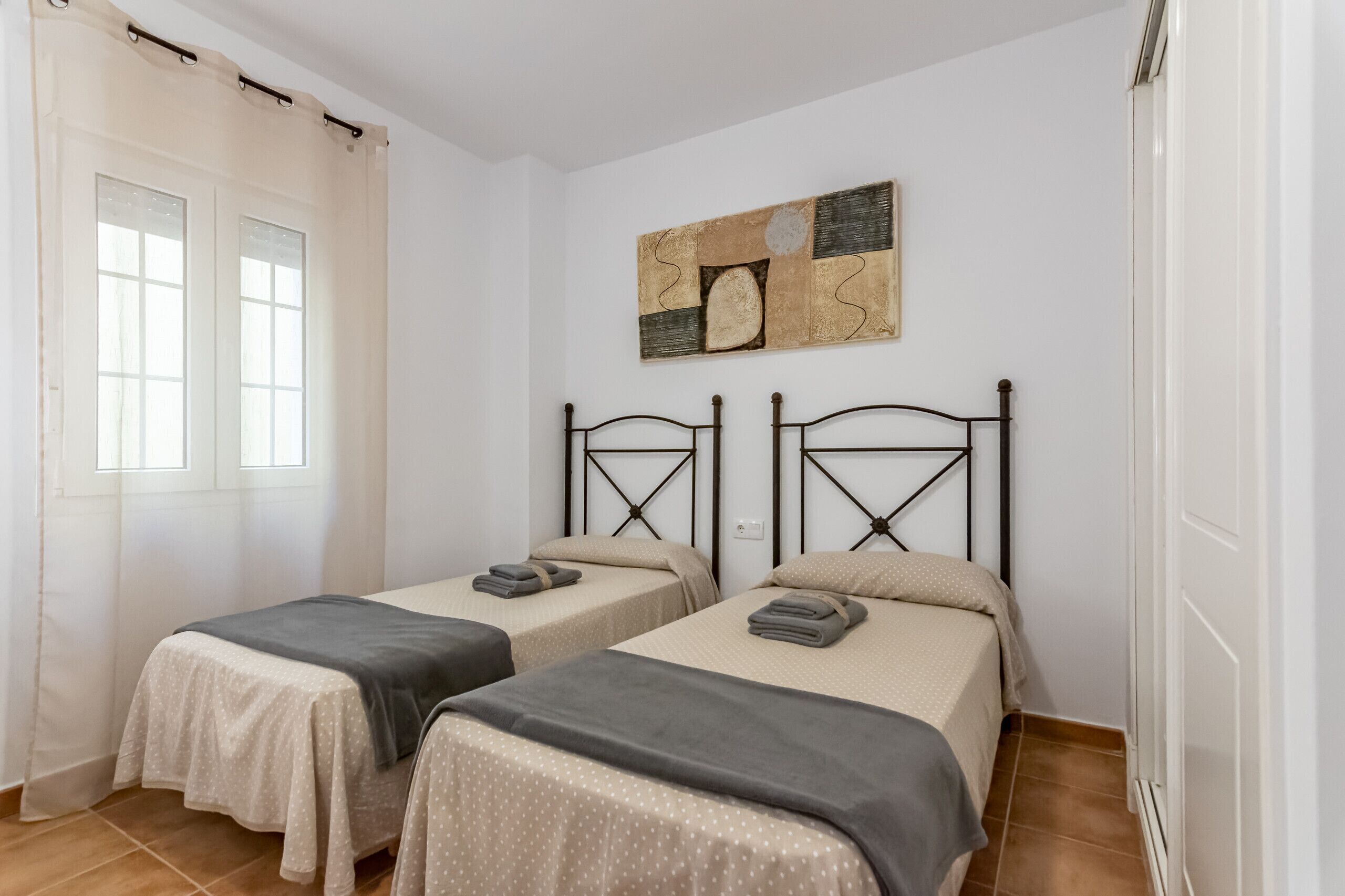 A room with two single beds, a window with curtains, a wall-mounted abstract art piece, and a radiator.