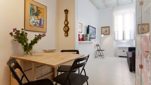 A dining area with a wooden table and black chairs, a vase with flowers, a wall clock, and a painting.