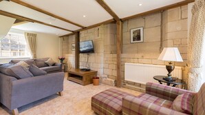 A cozy living room with a stone wall, a flat-screen TV, a fireplace, and a comfortable seating area. - A sudeley castle cottage that sleeps 4 guests  in 2 bedrooms (Cheltenham)