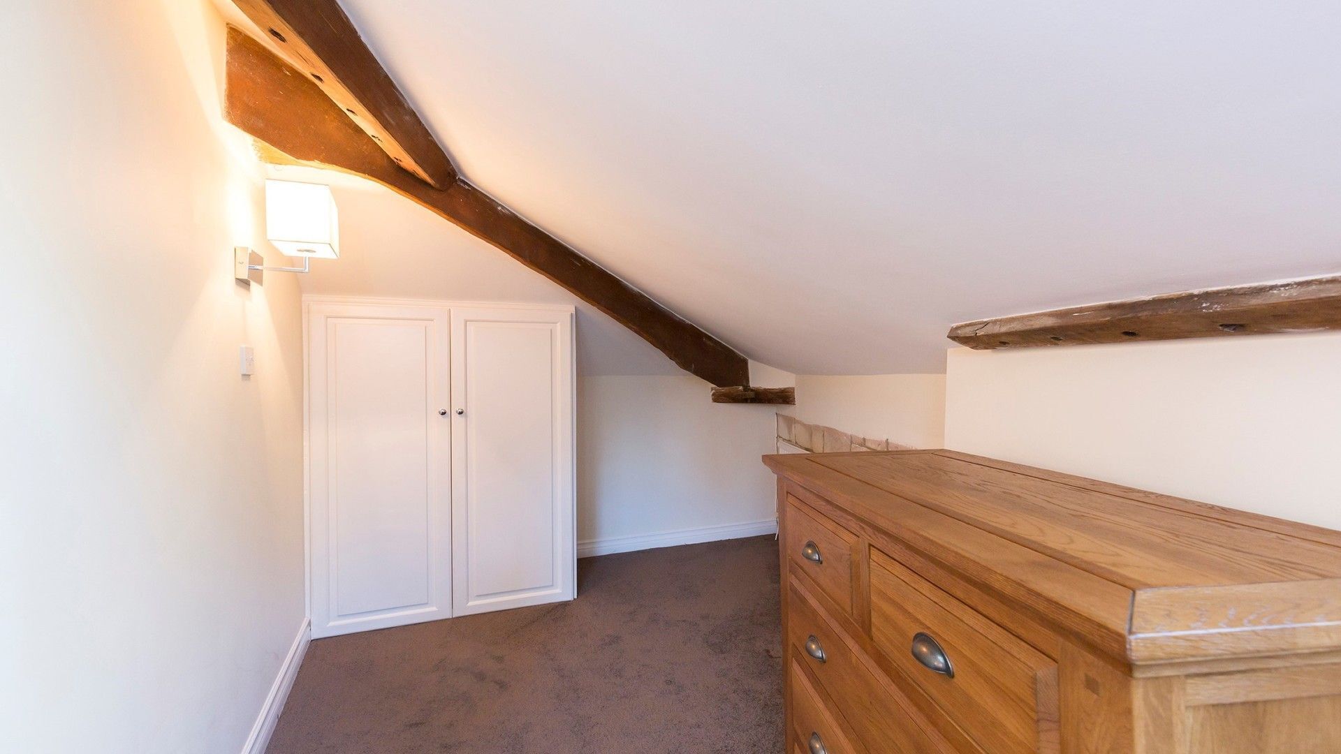 Une pièce avec une commode en bois, une porte double blanche et un plafond en pente avec des poutres apparentes.