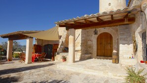 A stone building with a wooden door, a covered patio with tables and chairs, and a small tower. - Lovely Villa with swimming pool, BBQ, Wifi, Terrace, Patio, Garden, Fireplace,  (Porreres)