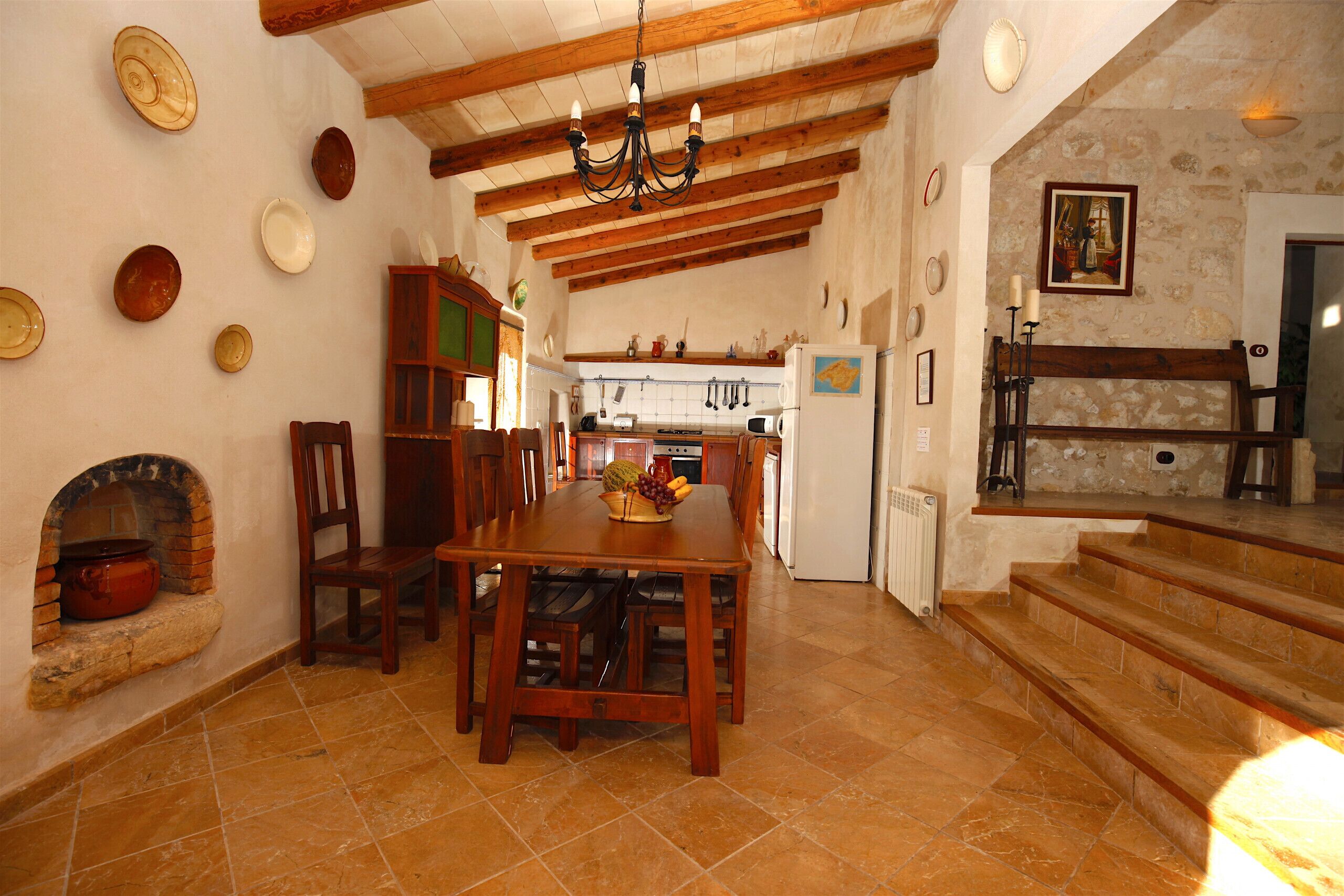 A rustic kitchen with wooden beams, a dining table with chairs, and a stone fireplace.