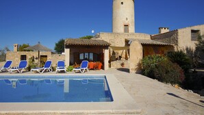 A pool area with lounge chairs, a stone building with a tower, and a clear blue sky. - Lovely Villa with swimming pool, BBQ, Wifi, Terrace, Patio, Garden, Fireplace,  (Porreres)