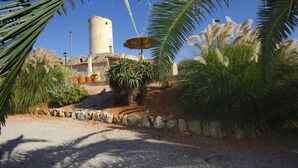 A courtyard with a stone pathway, palm trees, and a tower structure. - Lovely Villa with swimming pool, BBQ, Wifi, Terrace, Patio, Garden, Fireplace,  (Porreres)