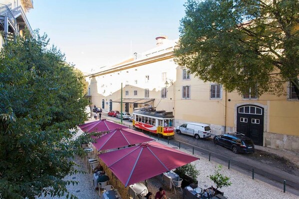 A tram passing by a row of buildings with outdoor seating areas.