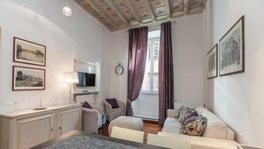 A compact living room with a sofa, a small table, a TV, and a window with curtains. - Frattina Exclusive Apartment (Rome)